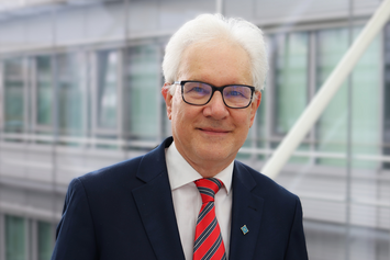 Vladimir Fomin Portrait of theoretical physicist Prof. Vladimir Fomin at IFW Dresden in front of a modern glass-and-steel interior. He is wearing a dark suit, a white dress shirt, and a red striped tie.