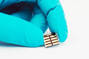 A gloved hand holding a small perovskite solar cell.
