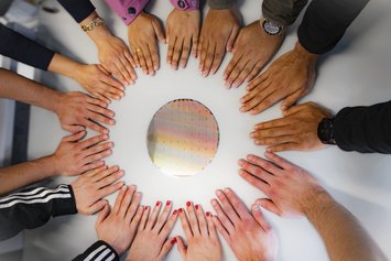 Gemeinsam. Viele Hände unterschiedlicher Hautfarbe bilden einen Kreis um einen runden glänzenden Wafer.